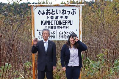 旧駅跡看板を背景に、村長と住民有志代表が「石」をPR